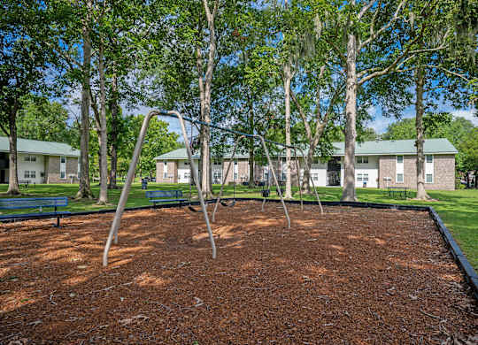 A playground with a red surface and a swing set. at Sawbranch Apartments, Summerville, SC, 29485
