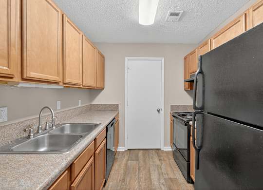 A kitchen with a black refrigerator and wooden cabinets at Sawbranch Apartments, Summerville, SC
