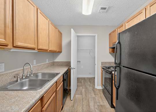 A kitchen with a black refrigerator, sink, and wooden cabinets at Sawbranch Apartments, Summerville