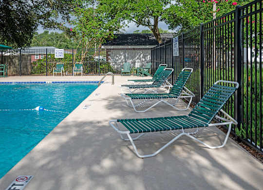 A pool with green chairs and a black fence at Woodlocke Apartments, Moncks Corner, SC, 27461