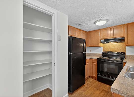 A kitchen with a black refrigerator and wooden cabinets at Woodlocke Apartments, South Carolina, 27461