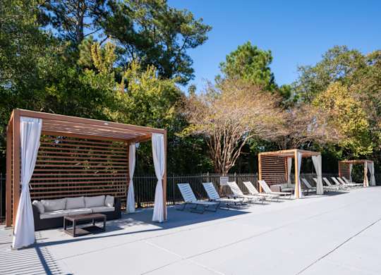 A sunny day at a poolside with a white couch and chairs at The Preserve at Pine Valley Apartments, Wilmington