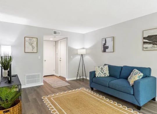 A blue couch with a white pillow is in the middle of a room with a rug at The Preserve at Pine Valley Apartments, Wilmington, NC 28412