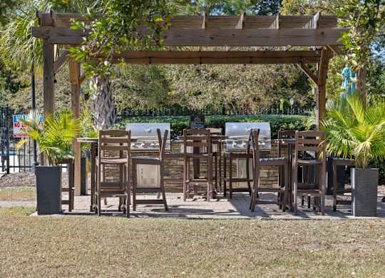 A wooden pergola with chairs and tables is surrounded by greenery at The Preserve at Pine Valley Apartments, North Carolina
