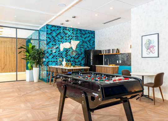 A foosball table is in the middle of a room with a blue tile wall behind it.at The Vale at the Parks, District of Columbia, 20012