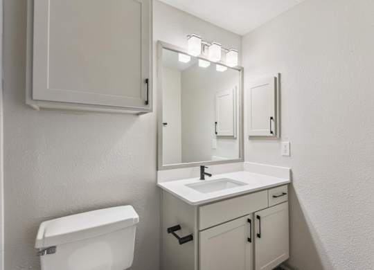 A white bathroom with a toilet, sink, and mirror.at Onyx183, Austin Texas  