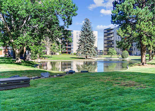 A park with a pond, trees and buildings in the background. at The Lex At Lowry, Denver, 80224