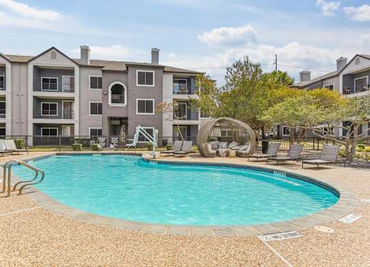 A large swimming pool is surrounded by a concrete patio and chairs.at Onyx183, Austin Texas  