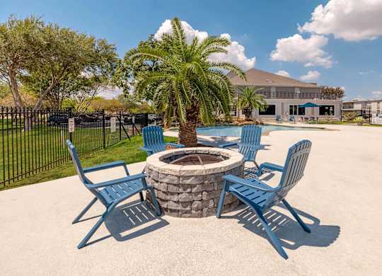 A fire pit surrounded by blue chairs in a sunny outdoor setting.