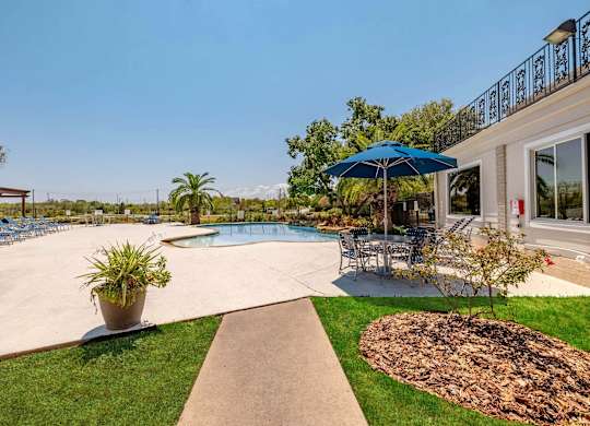 A pool area with a blue umbrella and a concrete walkway.