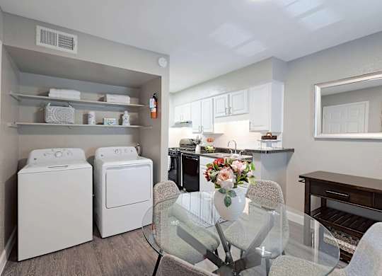 A laundry room with a washer and dryer, a dining table with chairs, and a kitchen area with cabinets and a countertop.