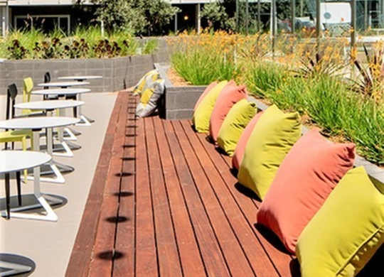A wooden bench with orange and green cushions is in front of a building.at Prizma, Los Angeles  