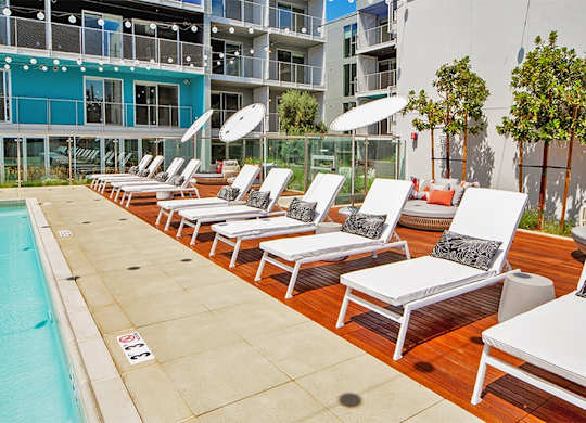 A row of sun loungers are set up on a wooden deck next to a pool.at Prizma, Los Angeles, 90038  