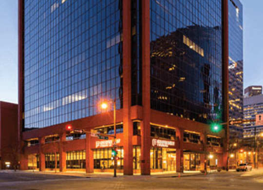 A tall glass building with a red frame stands in the evening sunlight.