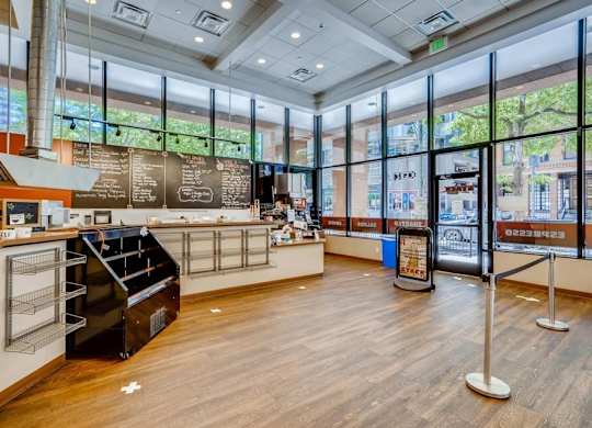 The image shows a spacious interior of a building with a counter, a chalkboard menu, and a view of the outside through large windows.