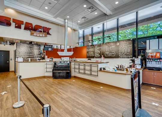 The image shows the interior of a Stack Subs restaurant with wooden floors and a counter with a menu board.