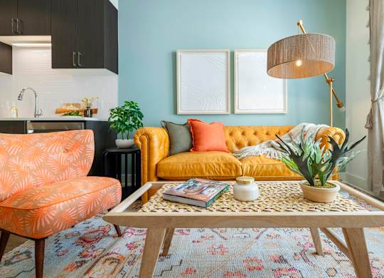 A living room with a yellow sofa, a patterned rug, and a wooden coffee table.at The Vale at the Parks, Washington, DC  