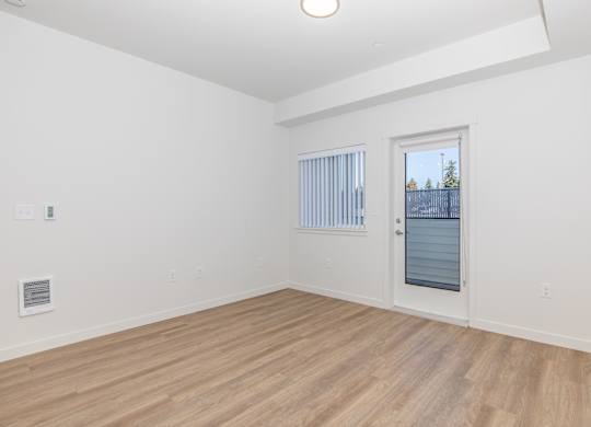 A room with a wooden floor and a window with a view of a fence and trees.