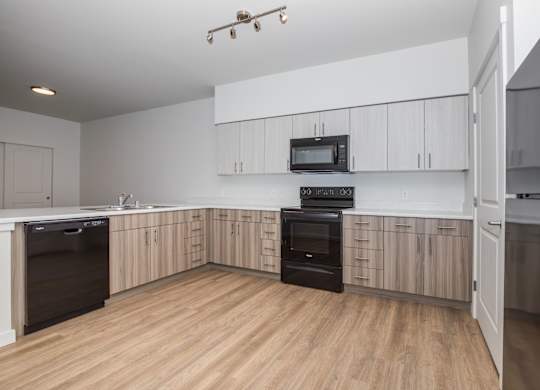 A modern kitchen with wooden floors and black appliances.