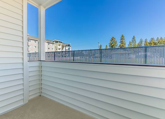 A balcony with white walls and a black railing overlooks a residential area.