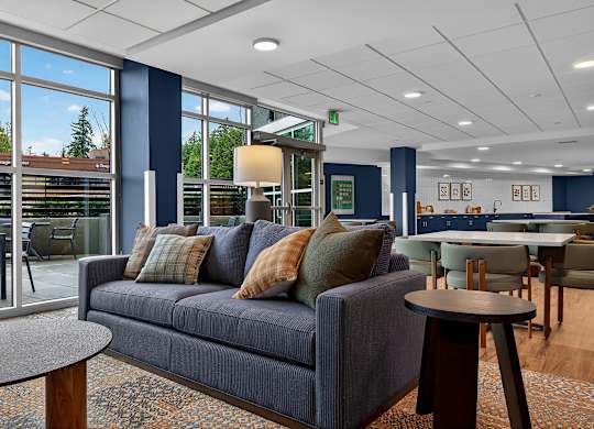 A grey couch with pillows sits in a room with a table and chairs.