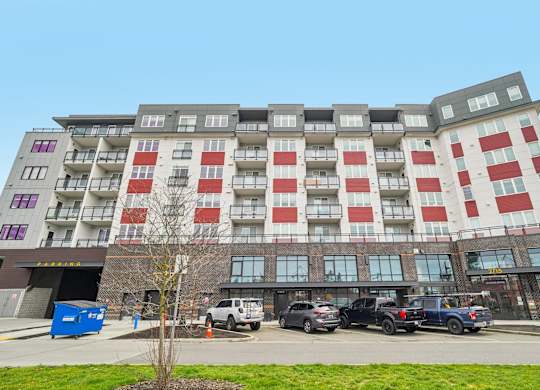 A large building with red and white balconies is surrounded by parked cars.