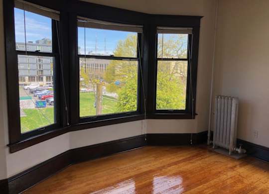 A room with wooden floors and a large window overlooking a parking lot.