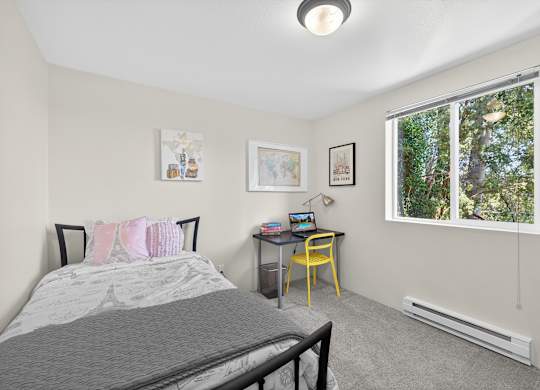 A bedroom with a bed, desk, chair, and pictures on the wall.