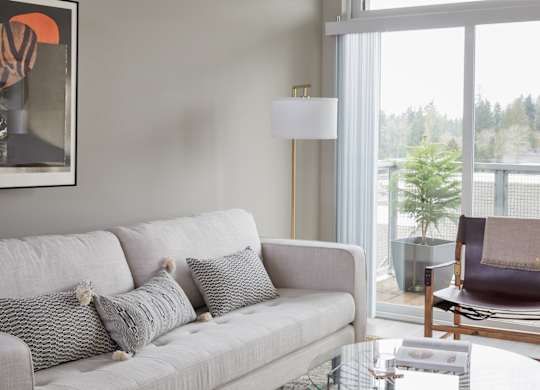 A grey couch with two pillows and a small table with a lamp on it.