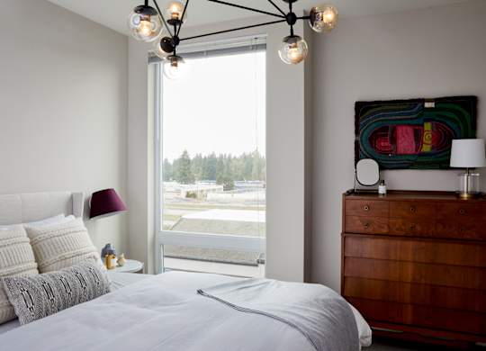 A bedroom with a large bed, a wooden dresser, and a window overlooking a parking lot.