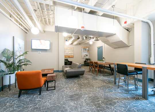 A modern office space with a patterned carpet and a mix of orange and black furniture.