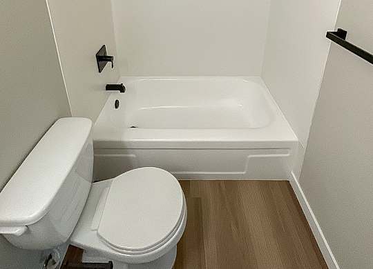 A white toilet sits next to a white bathtub in a small bathroom.