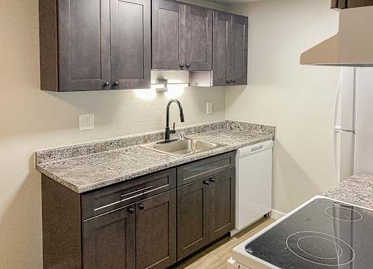 A kitchen with a granite countertop and dark brown cabinets.