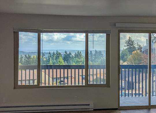 A room with a view of a forest and a building through the windows.