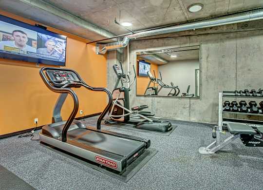 A treadmill in a gym with a TV screen showing two people.