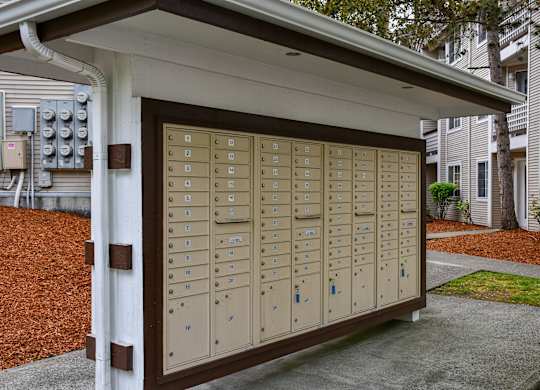 A brown mailbox with a white roof is in front of a building.
