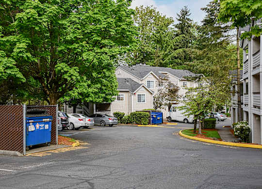 A parking lot with a blue recycling bin and a white car parked in front of a house.