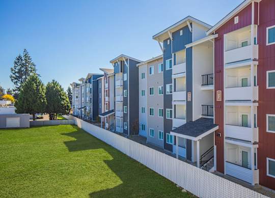 A row of modern apartment buildings with balconies and a green lawn in front.