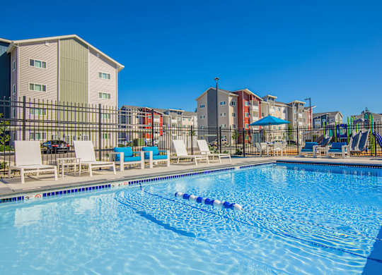 A swimming pool with lounge chairs and a playground in the background.