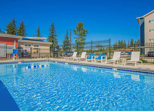 A large blue swimming pool with white lounge chairs and a fence around it.