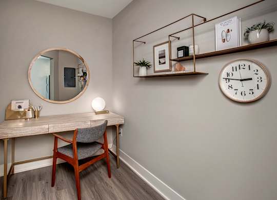 A wooden desk with a chair and a round mirror on the wall.