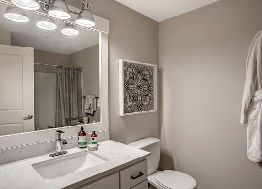 A bathroom with a toilet, sink, mirror, and a picture on the wall.