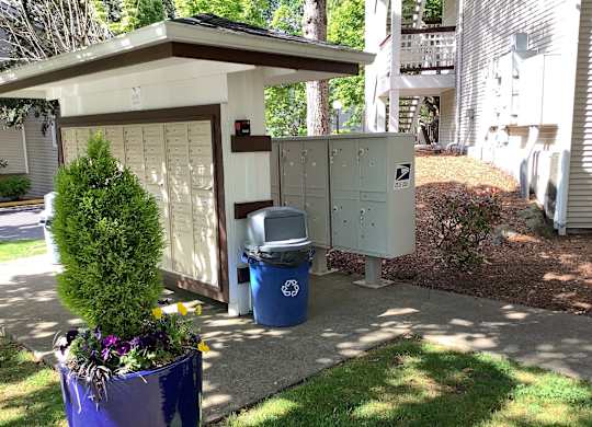 A mailbox is next to a trash can and a mailbox is on the other side of the fence.
