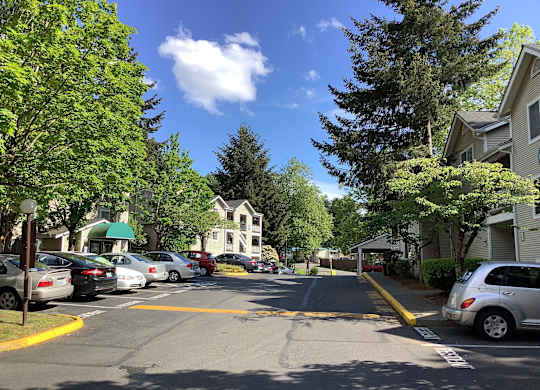 A street view with cars parked on the side and a white building in the background.