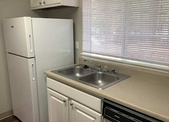A white refrigerator stands next to a sink in a kitchen.