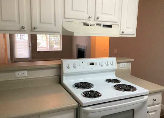 A white stove with four burners is in a kitchen with white cabinets.