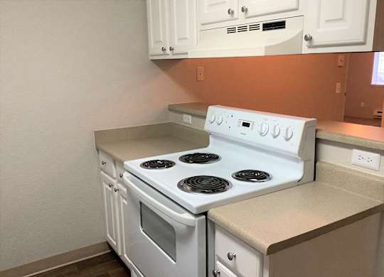 A white stove top oven with four burners and a white dishwasher in a kitchen.