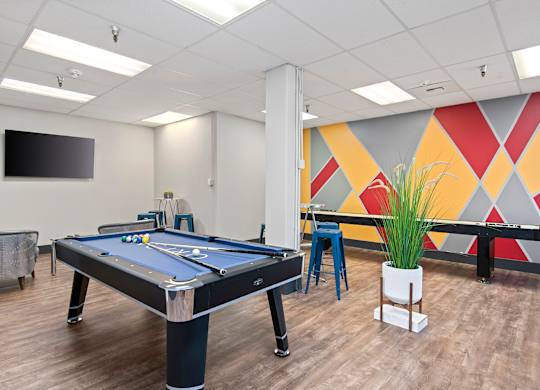 A pool table in a room with a TV mounted on the wall.
