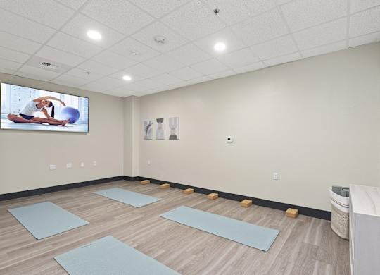 A yoga studio with mats on the floor and a TV screen showing a yoga class.
