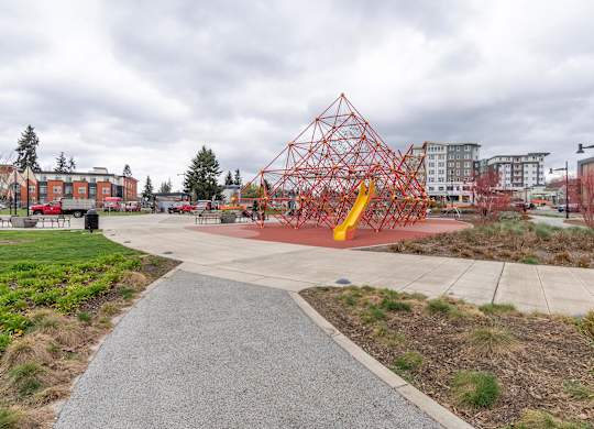 A playground with a red and yellow structure in the middle of a concrete area.